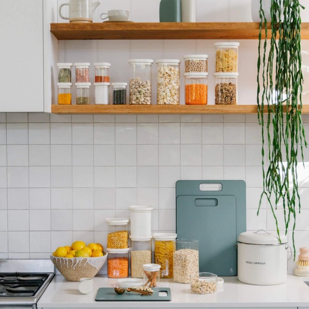 Glassbeholdere med hvite glasslokk fylt med tørrvarer på åpne kjøkkenhyller og benk – ryddig, plastfri pantryorganisering fra Seed & Sprout.