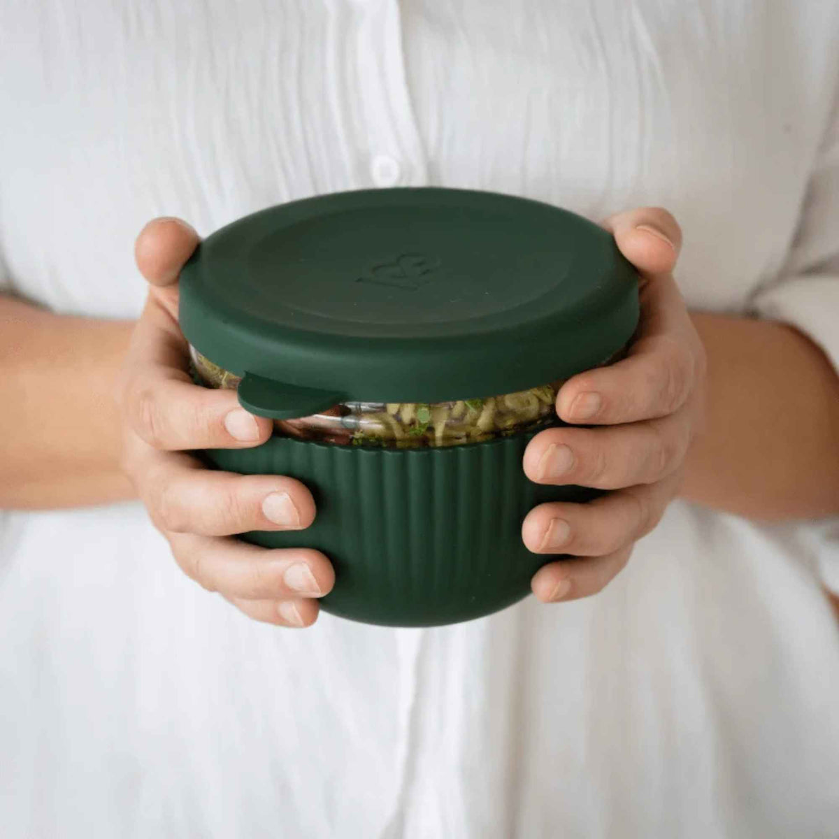 Person holder en lukket matboks i borosilikatglass med silikonbeskyttelse og lekkasjesikkert lokk i fargen Moss.