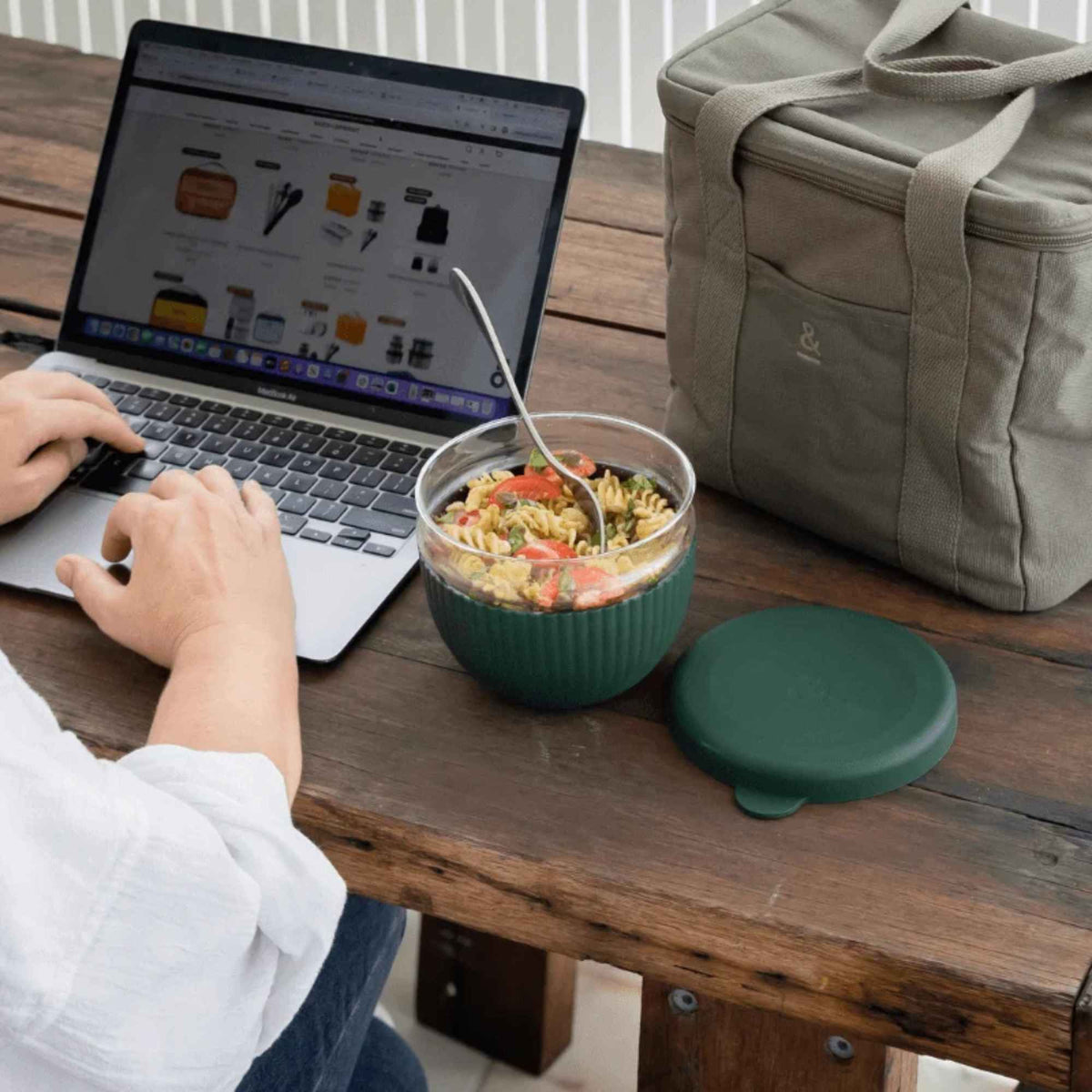 Matboks i borosilikatglass med pastasalat ved siden av en laptop og kjølebag, med silikonlokk i fargen Moss.