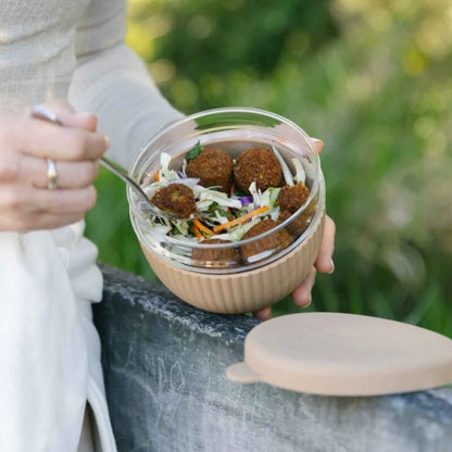 Person spiser salat fra en matboks i borosilikatglass med silikonbeskyttelse og lokk i fargen Praline.