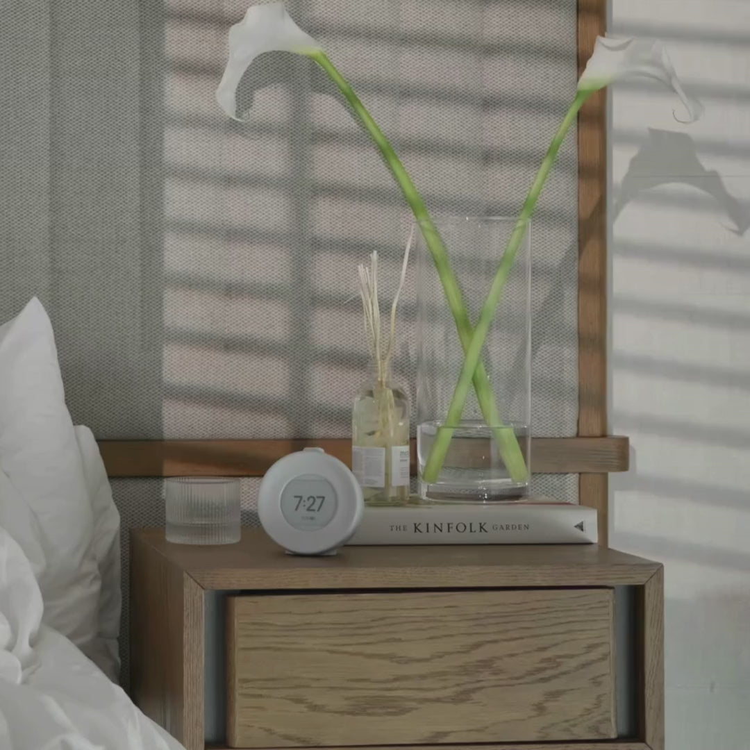 Video som viser Mudita Harmony Pebble Grey vekkerklokke på nattbordet om morgenen, med naturlig lys og en rolig start på dagen for bedre søvn og velvære.