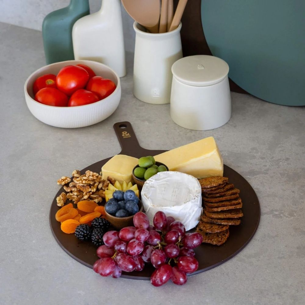 Rund skjærefjøl i trefiber med ost, kjeks og frukt på kjøkkenbenk, fra Seed & Sprout
