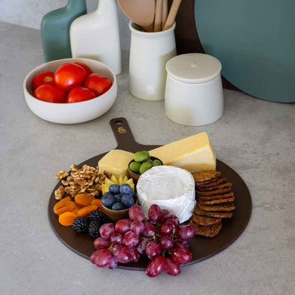 Rund skjærefjøl i trefiber i fargen Nutmeg brukt til servering av ost, kjeks, druer, nøtter og bær på kjøkkenbenk