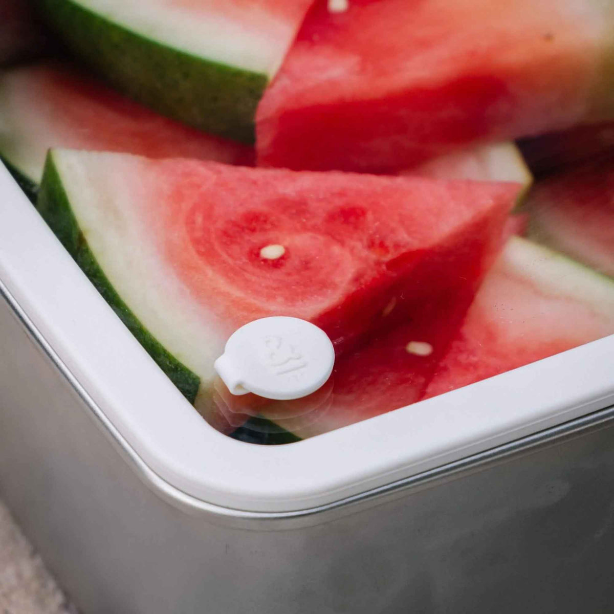 Nærbilde av silikonventilen og forseglingen på glasslokket til en matbeholder i rustfritt stål fra Seed & Sprout, fylt med vannmelon.