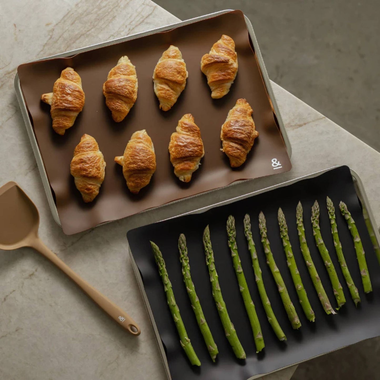 To silikonbakematter i fargene Clove og Liquorice, brukt til croissanter og ovnsbakt asparges, et gjenbrukbart non stick alternativ til engangs bakepapir.