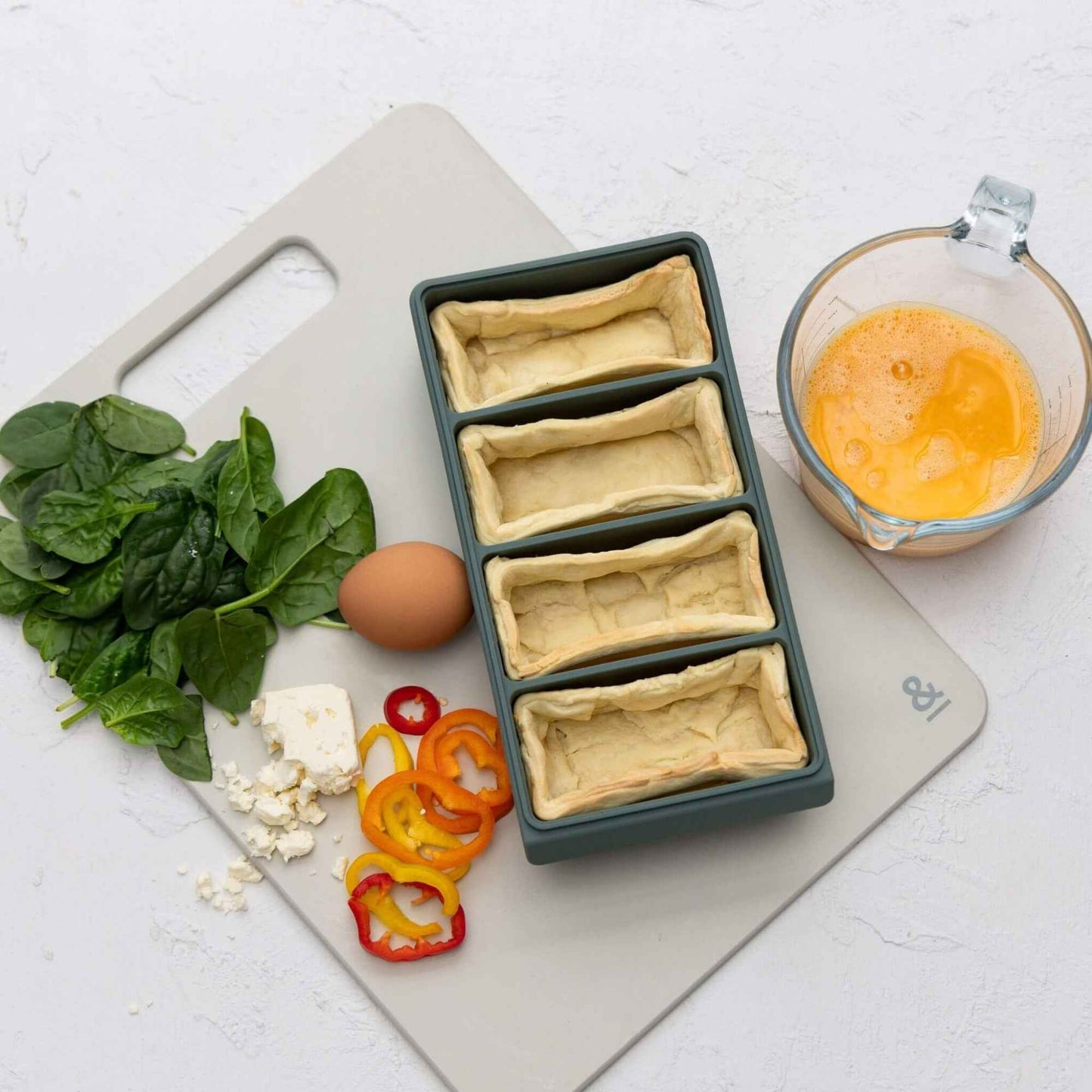 Silikon frysebrett med porsjonert deig på kjøkkenbenk med egg, paprika og grønnsaker klar til matlaging