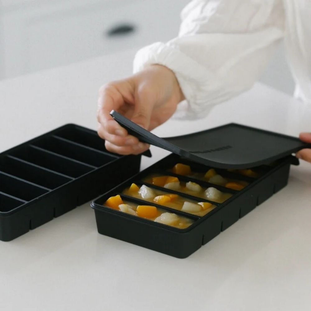 Silikon fryseform i svart LFGB-platinumsilikon der lokket løftes av for å vise seks små porsjoner med suppe.