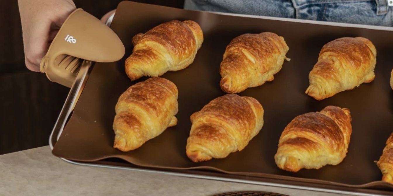 Nystekte croissanter på gjenbrukbar silikonbakematte, løftet ut av ovnen med grytevott i LFGB-sertifisert silikon fra Seed & Sprout.
