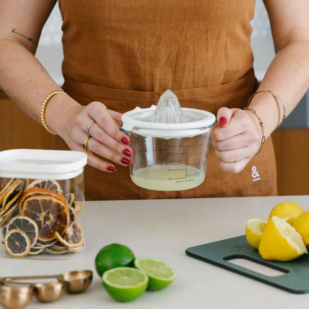 Sitruspresse i glass med målebeger, vist sammen med fersk sitron og lime.