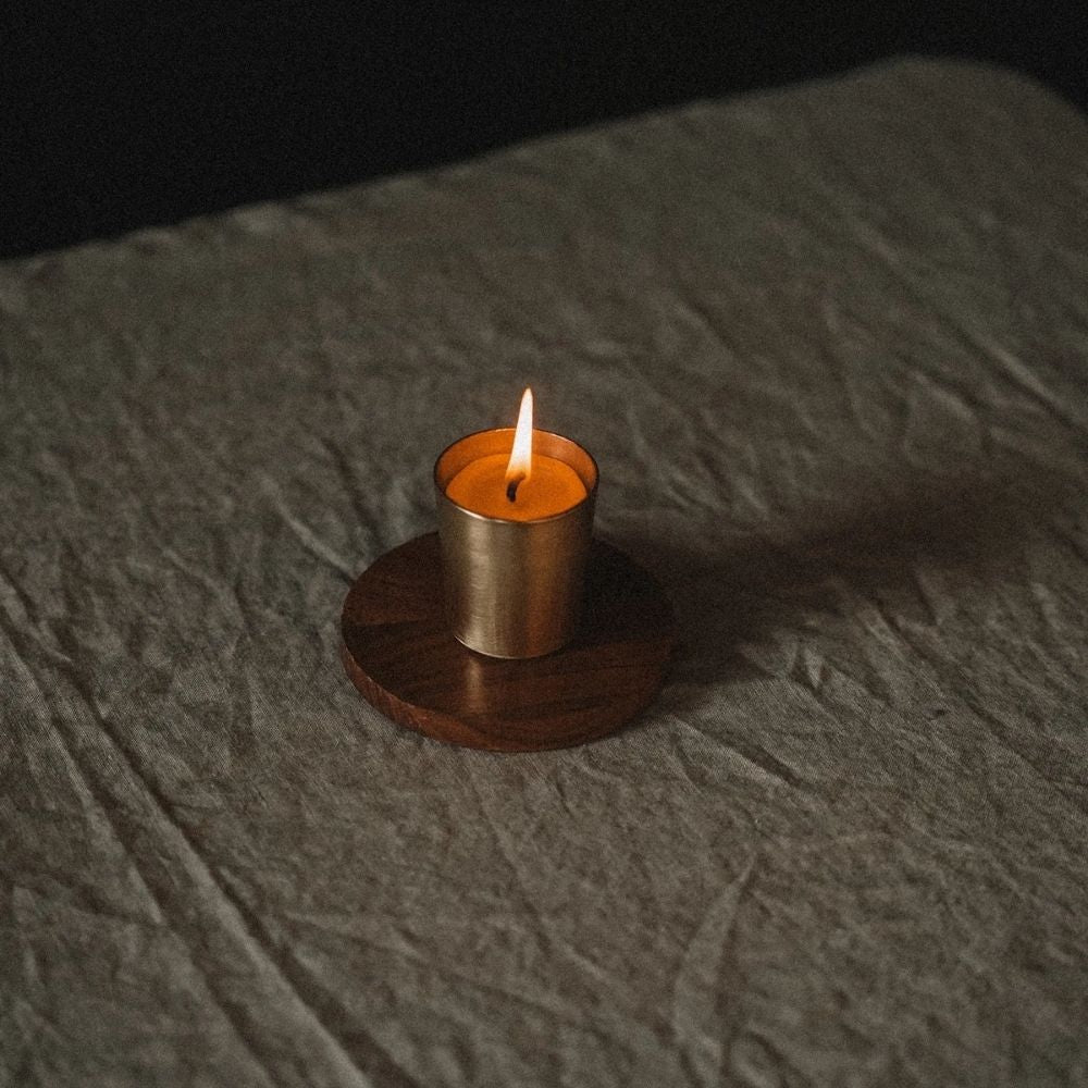 Tent Skär Organics bivokslys i gullfarget holder, plassert på treunderlag i varmt stemningslys – økologisk håndlaget bivokslys hos Sunnerhjem.