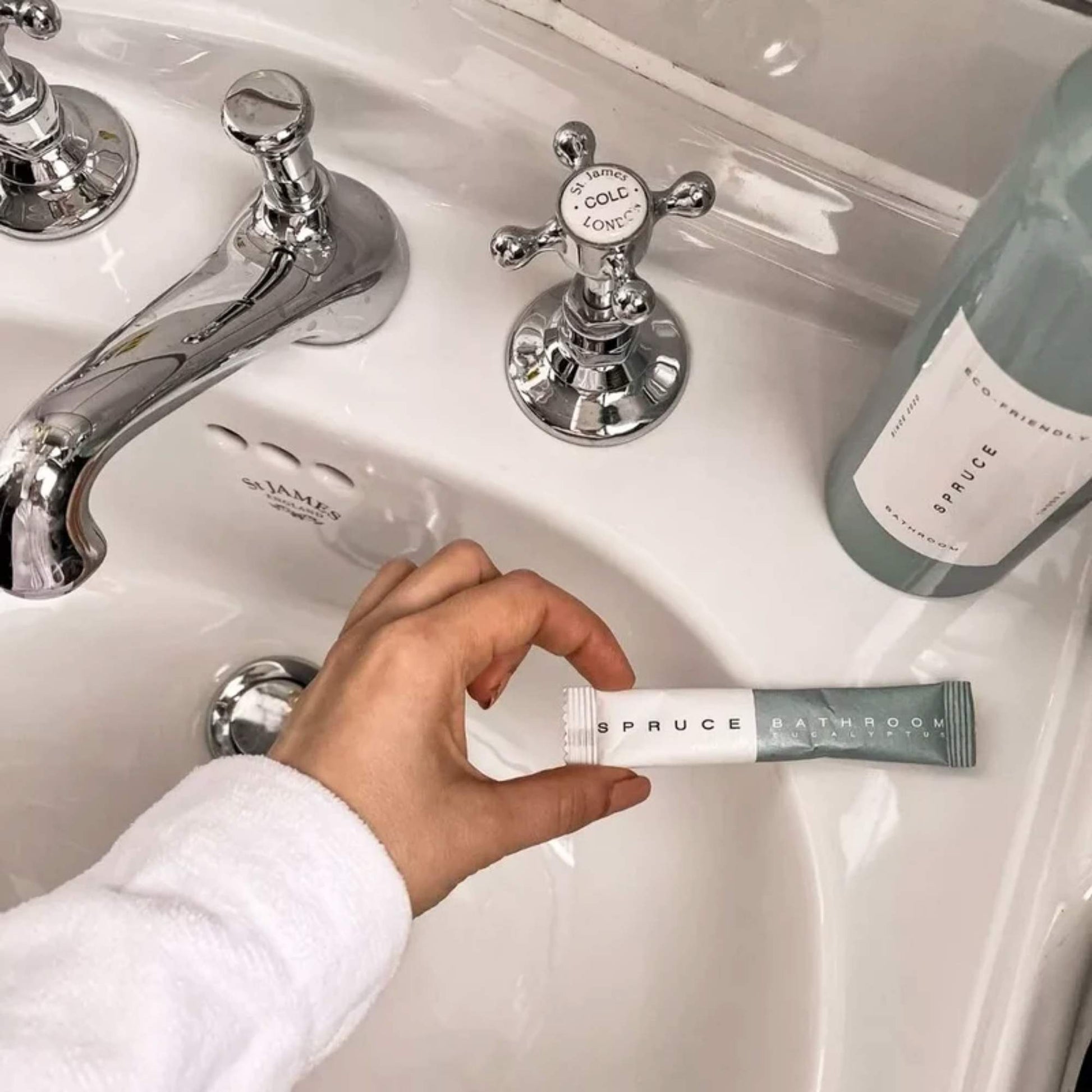 Spruce baderomsspray refill holdt over servant på bad, klar til å blandes i gjenbrukbar evighetsflaske