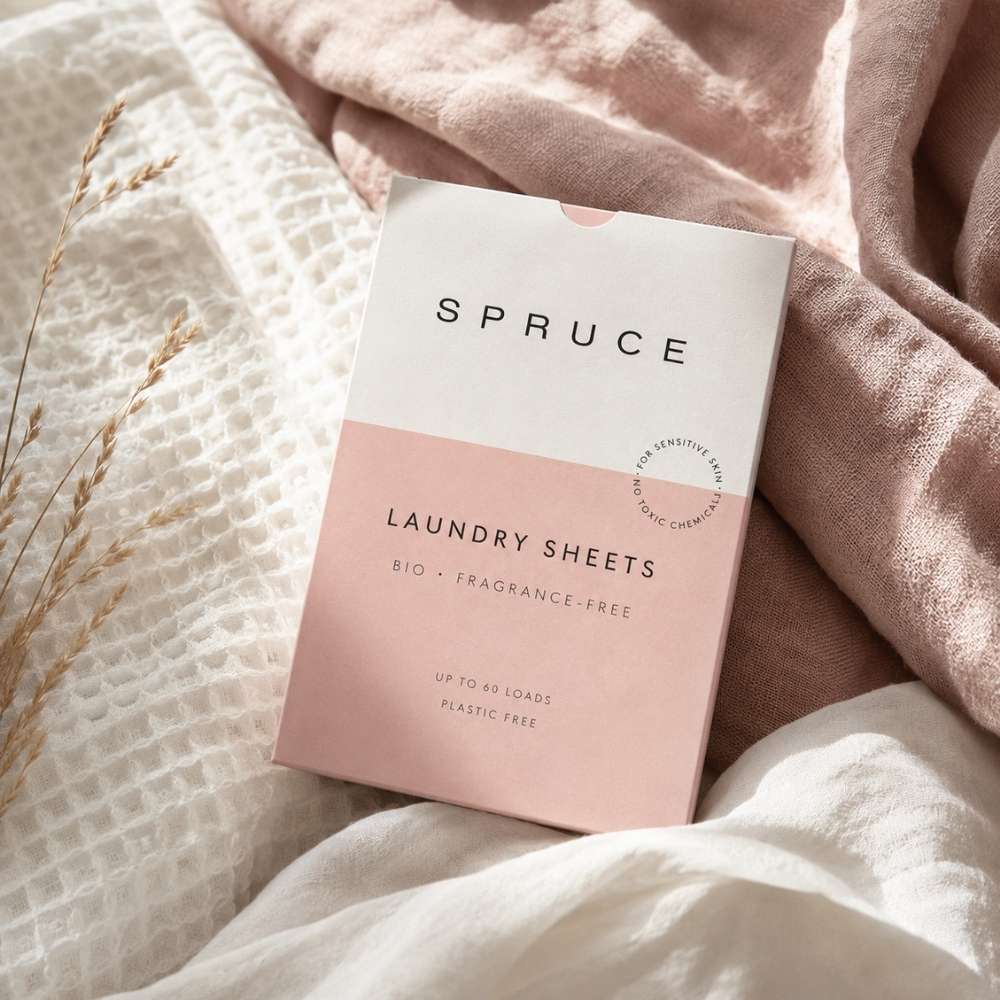 Spruce vaskeark plassert på myke naturlige tekstiler i lyse beige og rosa toner med varmt naturlig lys.