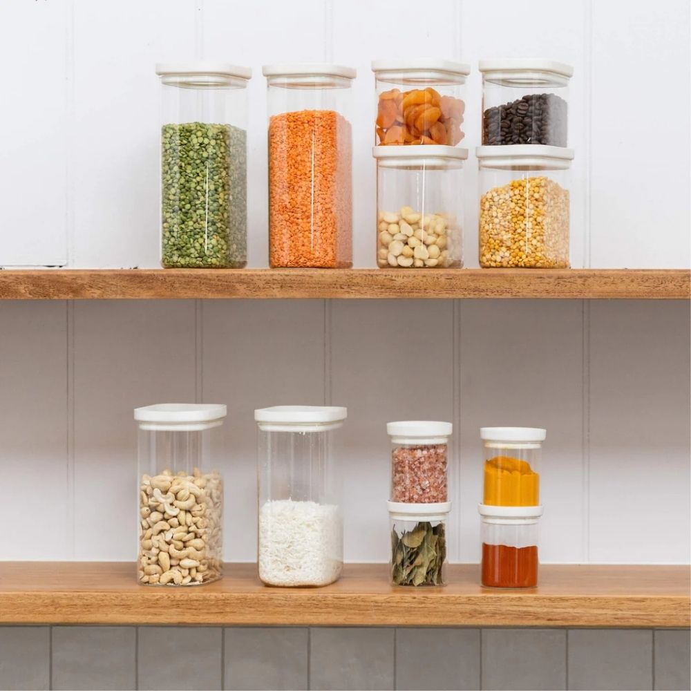Stabelbare krydderglass i glass med glasslokk fylt med krydder, linser og nøtter organisert på kjøkkenhylle for plastfri pantry-oppbevaring.