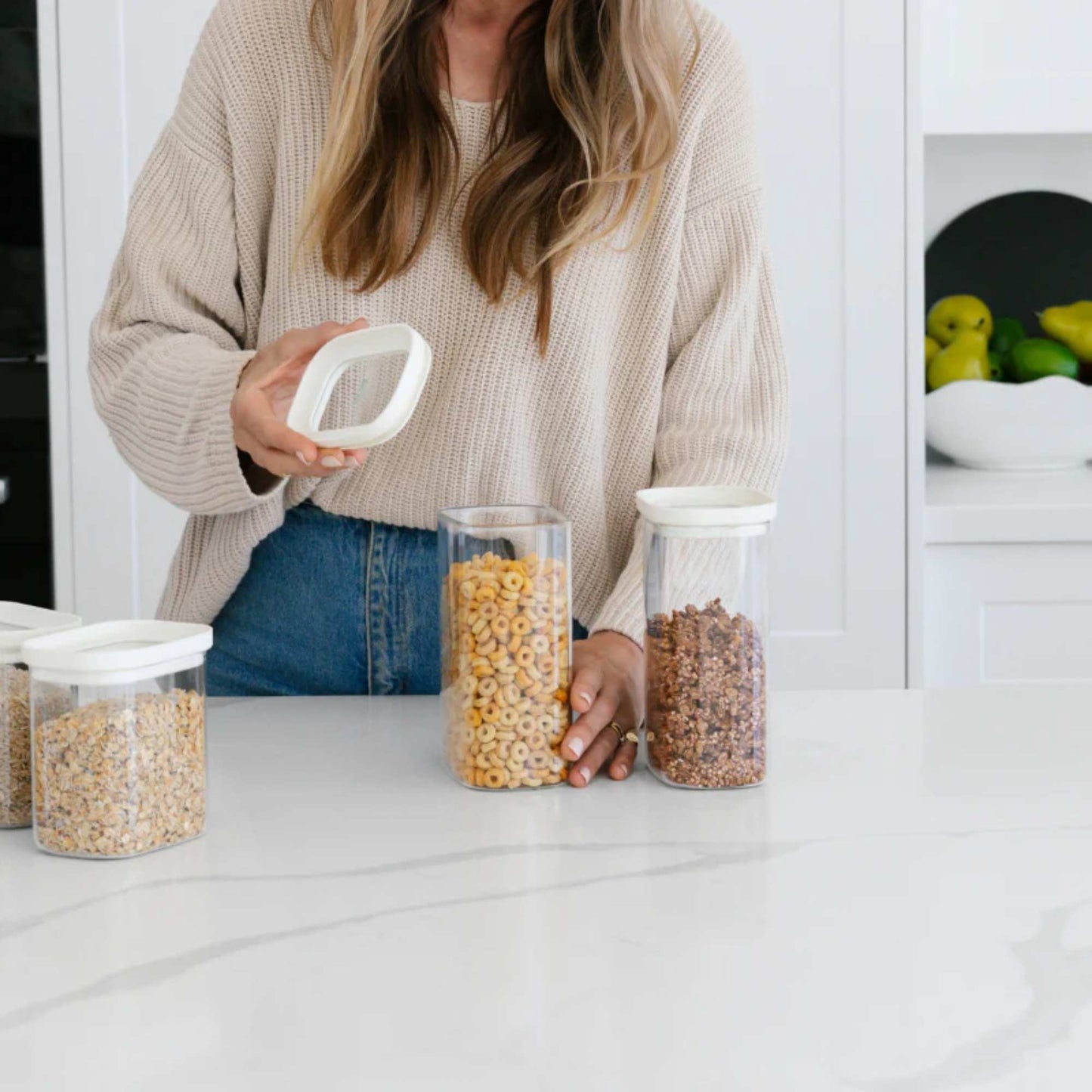 Kvinne fyller Tallow glassbeholdere med tørrvarer på kjøkkenbenken – plastfri og ryddig matoppbevaring.