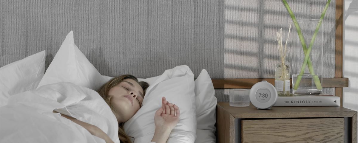 Kvinne som slapper av i sengen med Mudita Harmony lav-EMF alarmklokke på nattbordet i et teknologifritt soverom