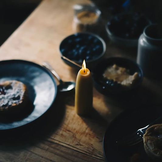 To økologiske stubbelys av bivoks skaper varmt og naturlig lys på et rolig frokostbord.