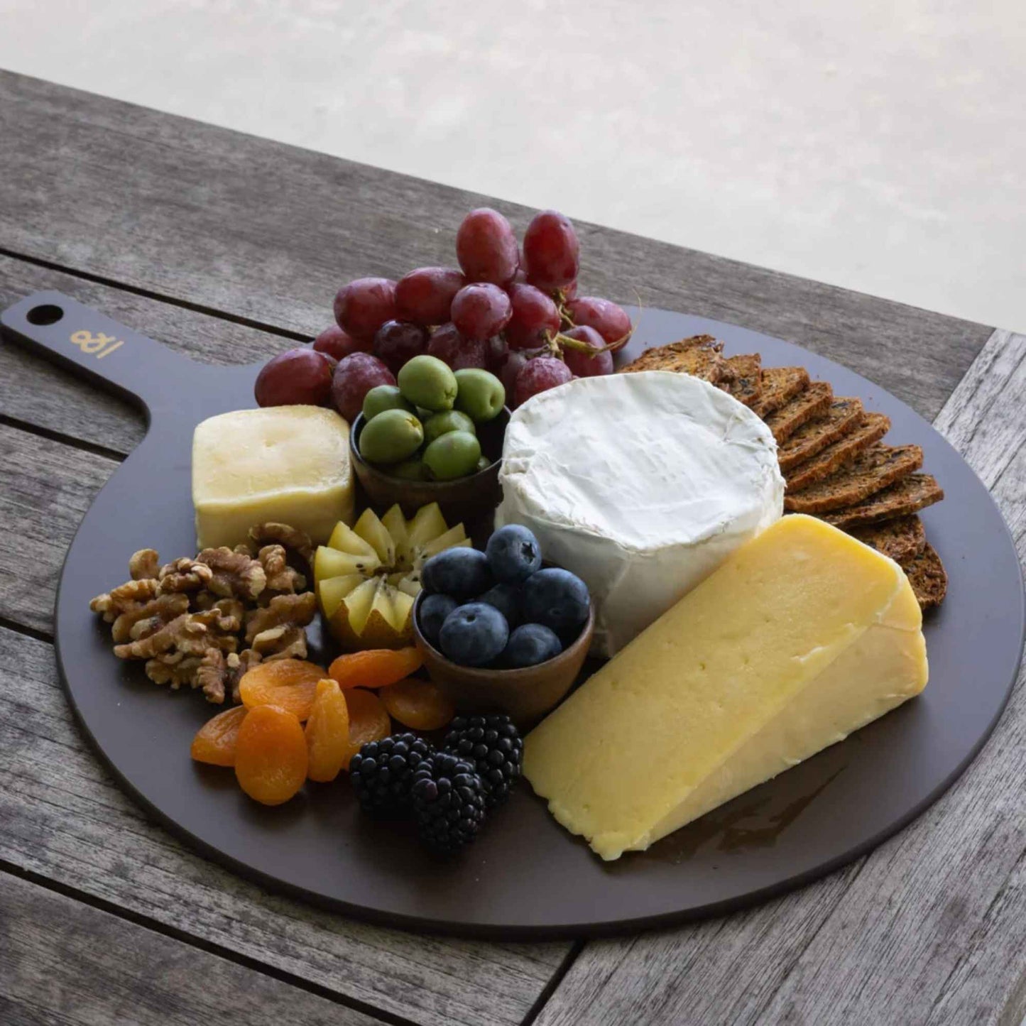 Rundt skjærebrett i trefiber fra Seed & Sprout brukt til servering av ost, frukt og nøtter utendørs