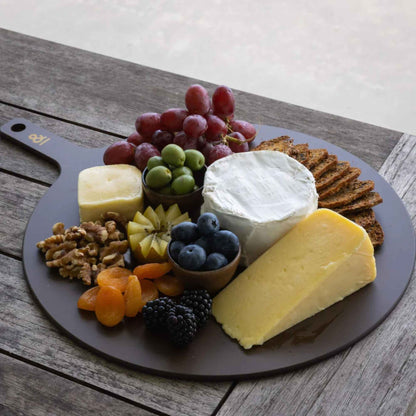 Rundt skjærebrett i trefiber fra Seed & Sprout brukt til servering av ost, frukt og nøtter utendørs