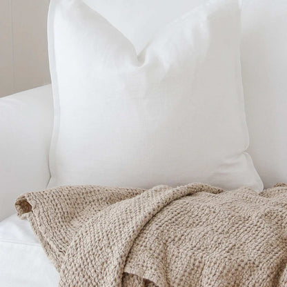 Beige waffle pledd i lin og bomull, elegant dandert over en sofa i en lys stue – mykt og stilrent interiørtilbehør