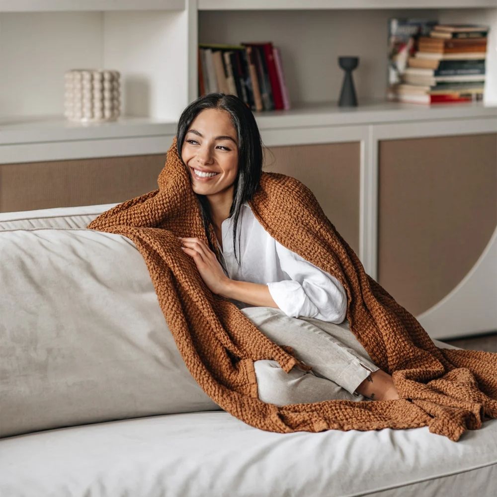 Kvinne med waffle-pledd i lin og bomull i fargen cinnamon rundt skuldrene, som viser pleddets myke tekstur og varme, naturlige uttrykk.