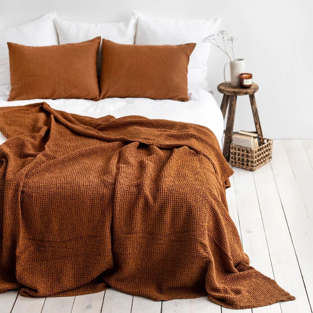 Waffle-pledd i lin og bomull i fargen cinnamon lagt på en seng, som viser den myke strukturen og den varme, naturlige fargetonen i soverommet.