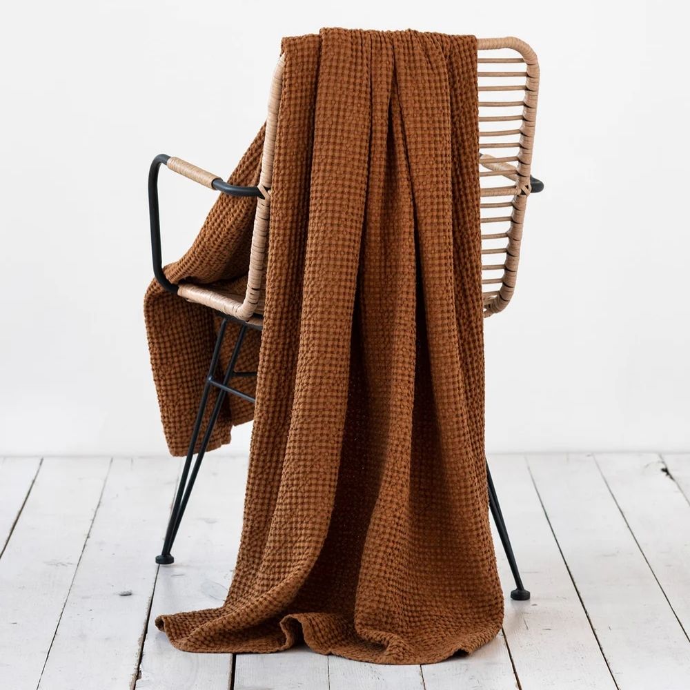 Waffle-pledd i lin og bomull i fargen cinnamon drapert over en stol, som viser den myke vaffelstrukturen og den varme, naturlige tonen i interiøret.