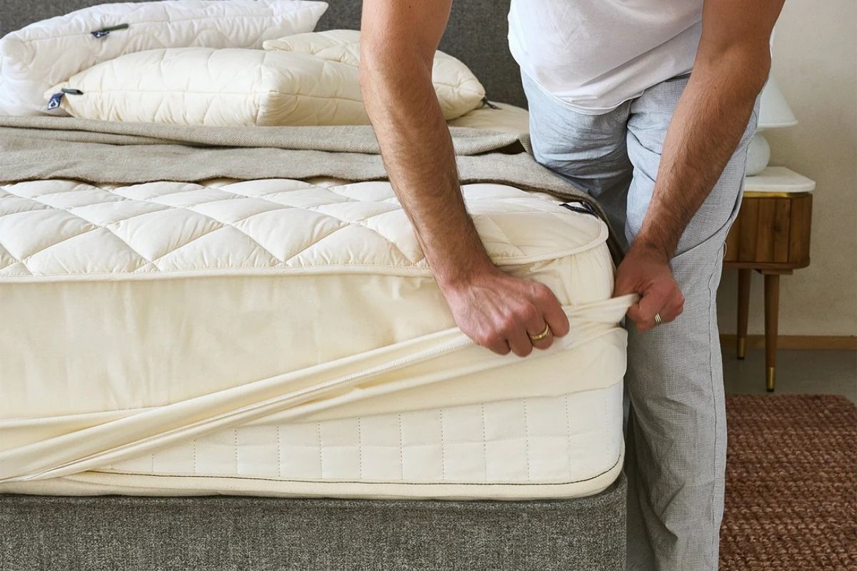 Person monterer temperaturregulerende madrassbeskytter i ull og økologisk bomull fra Woolroom på seng.